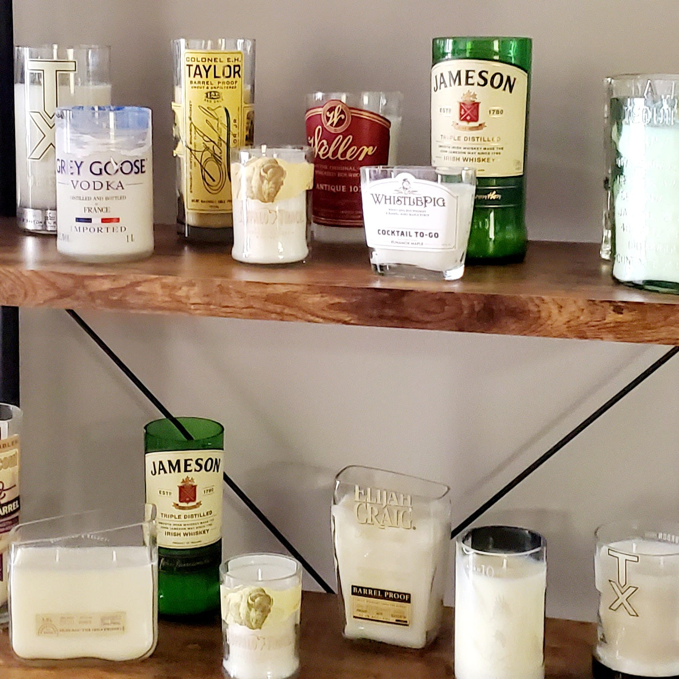 Hand cut liquor bottle candles lined up on wooden shelves in the SweetlyRecycled studio